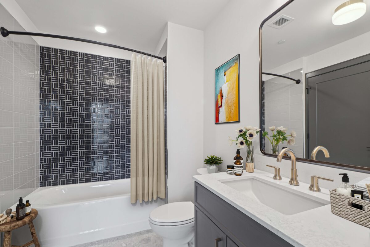 Modern bathroom with geometric tiled shower wall and marble vanity.