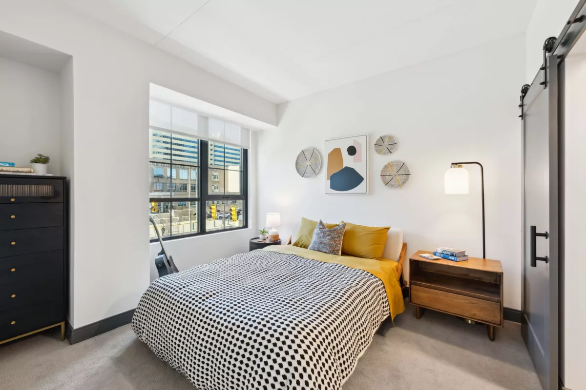 Bedroom with white walls, black-framed windows, and light colored carpet with a bed, dresser, and night stands
